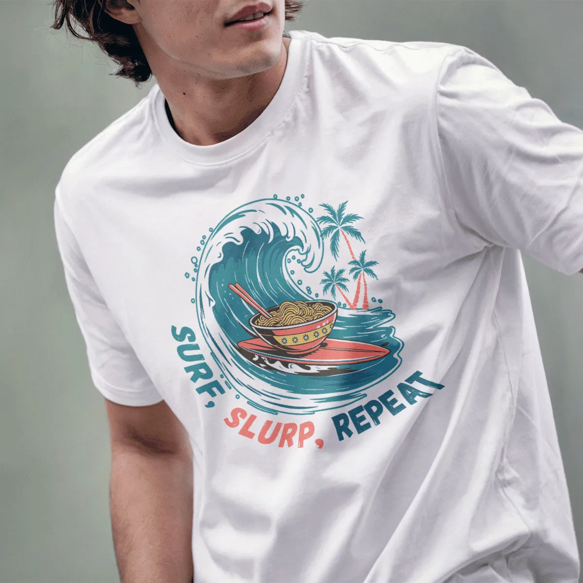Male model wears white t-shirt featuring vibrant ramen on surfboard, palm trees, and bold retro text.