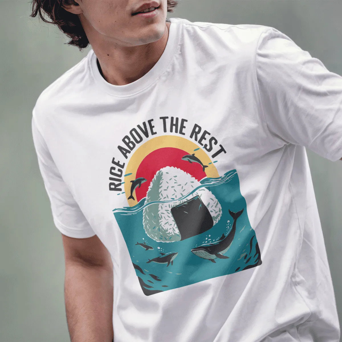 Male model wears white t-shirt featuring whimsical onigiri island, dolphins, whales, and “Rice Above the Rest” text.